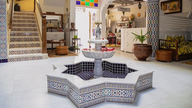 Um hall amplo com uma fonte central, uma escadaria com ladrilhos estampados e uma galeria com diversos objetos expostos.