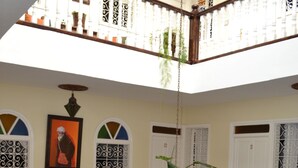 Interior com vários níveis, uma escada de madeira, guarda-corpos brancos e detalhes decorativos, incluindo uma moldura com imagem e plantas em vasos.