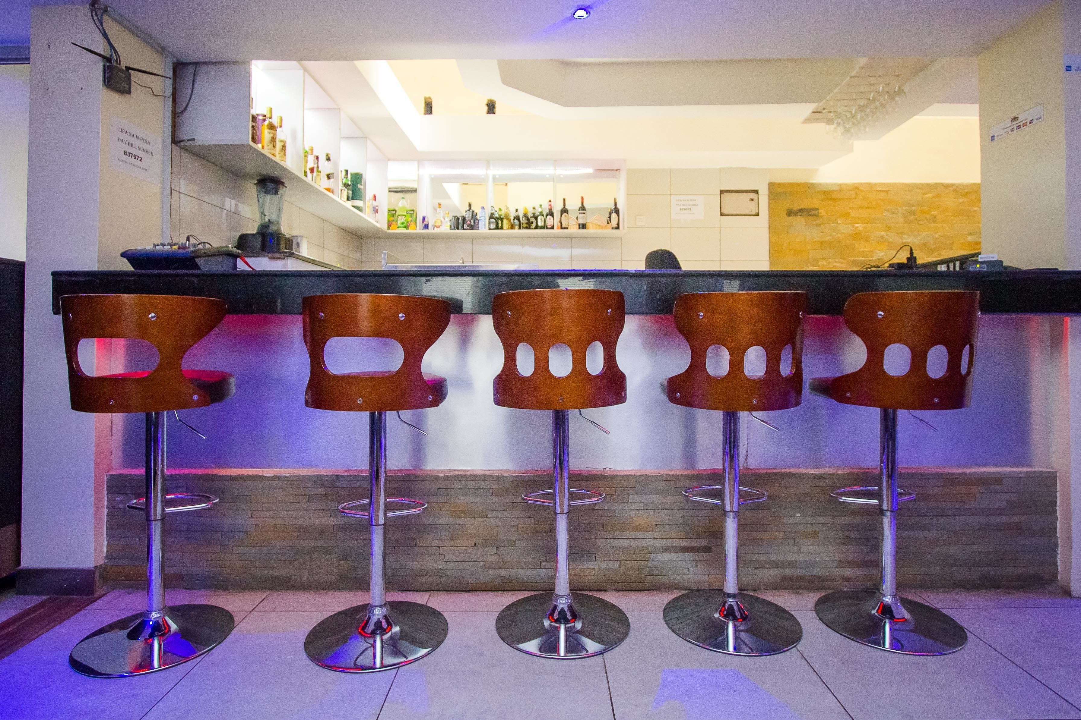 A bar area with five wooden bar stools and a counter with various bottles.