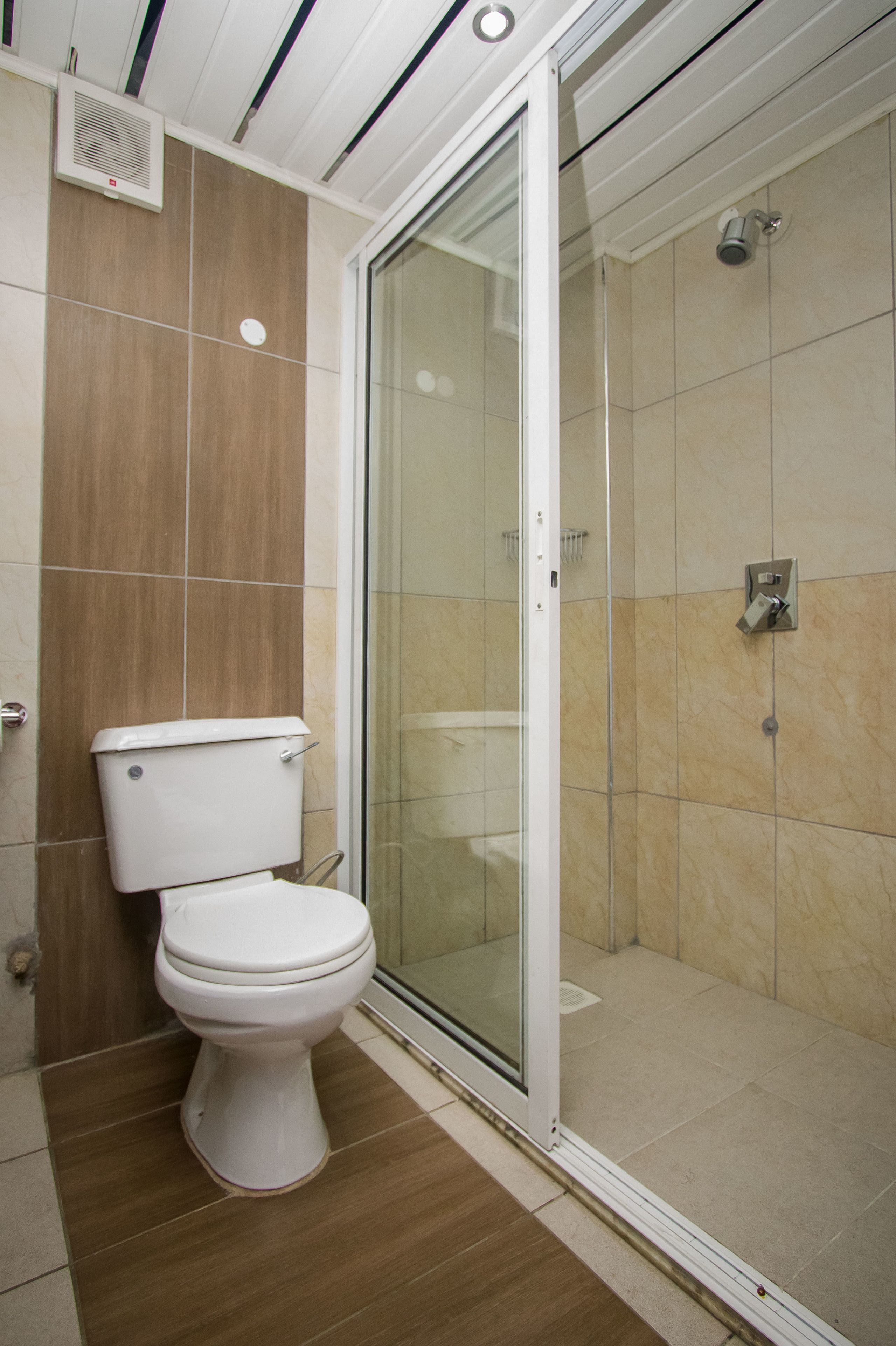 A bathroom with a toilet, a shower with a glass door, and a ventilation unit on the wall.