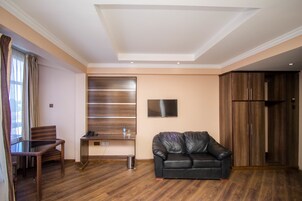 A modern living room with a glass dining table, a leather sofa, a TV mounted on the wall, and wooden cabinets.