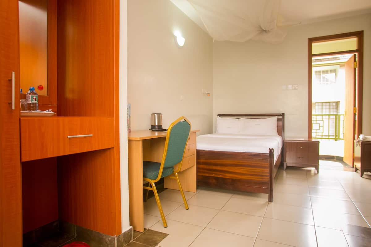 Una habitación con cama, escritorio, silla, armario y una mesita con una botella de agua.