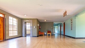 A spacious hallway with wooden flooring, a fire extinguisher, and a sign indicating a fire exit. - Desmond Tutu Conference Centre (Nairobi)