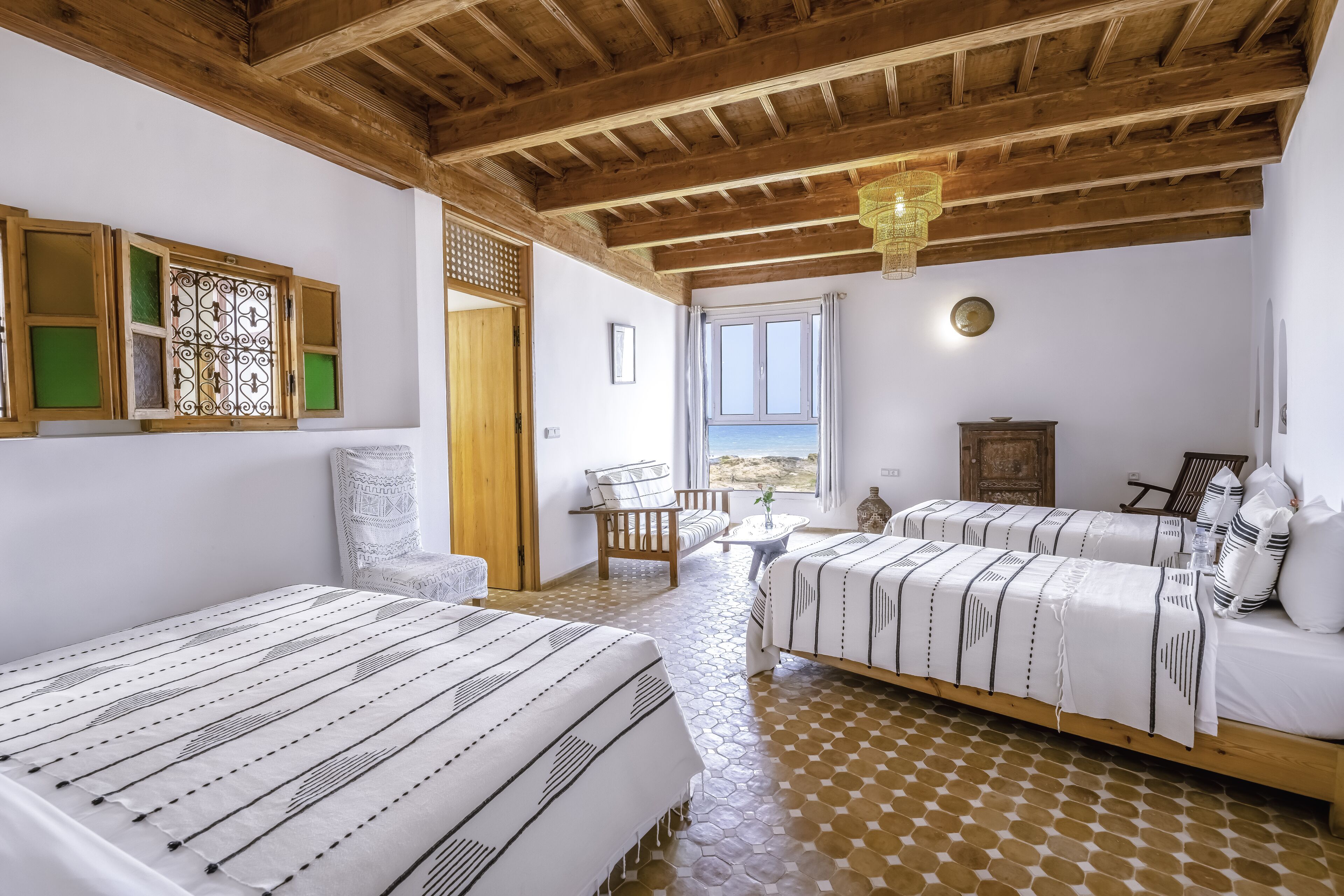 Un dormitorio con dos camas, vigas de madera, vistas al exterior y suelo estampado.