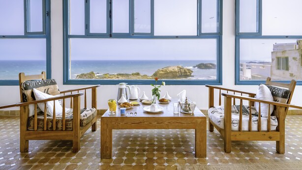 Una habitación con dos sillas de madera, una mesa de madera y un ventanal con vistas al mar.