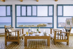 A room with two wooden chairs, a wooden table, and a large window overlooking the sea. - Riad Kafila (Essaouira)