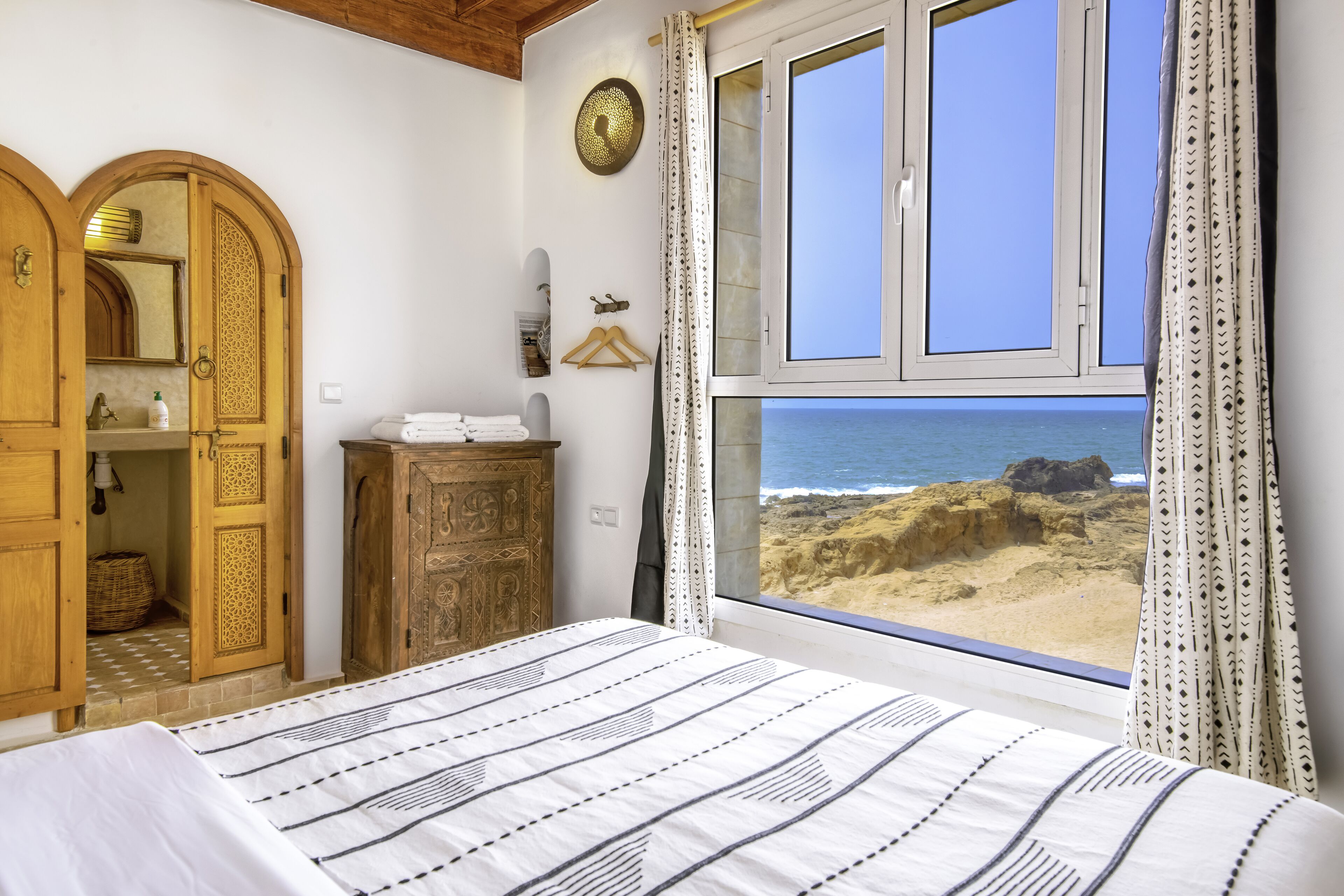 A bedroom with a bed, wooden wardrobe, and a window with a view of the beach.