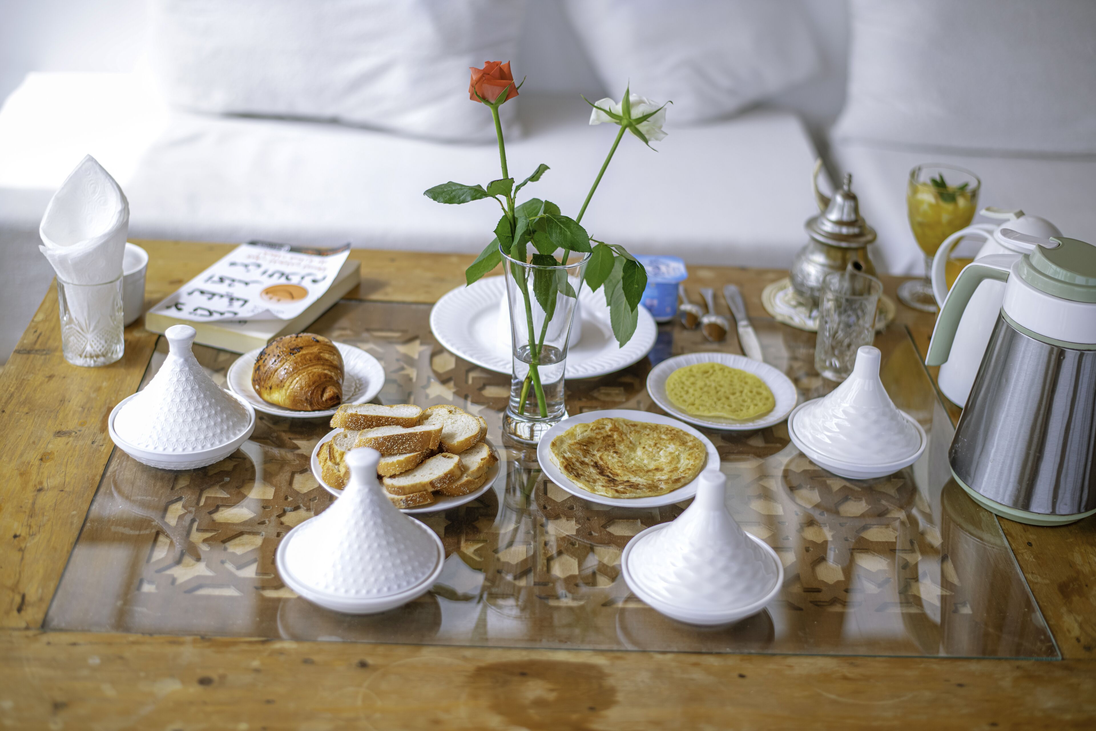 A breakfast table with various food items and a rose in a glass.