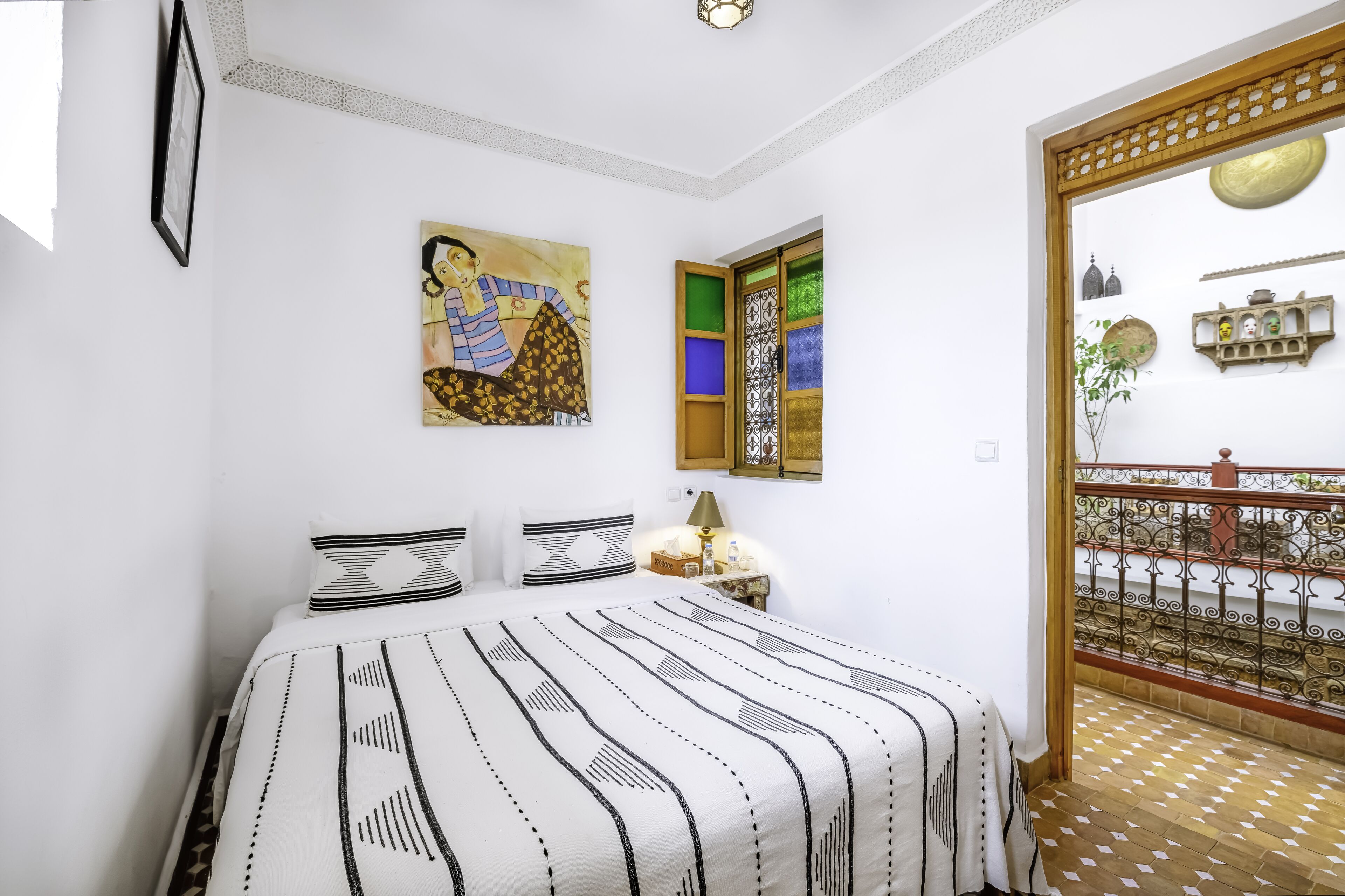 A bedroom with a bed, a painting, a nightstand, and a view of a balcony.