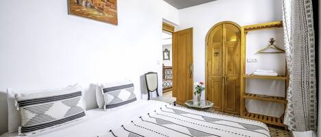 Un dormitorio con una cama grande, un armario de madera, una mesita con un jarrón y un cuadro en la pared.