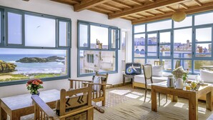 Una habitación acogedora con muebles de madera, ventanas amplias con marcos azules y vista al océano.