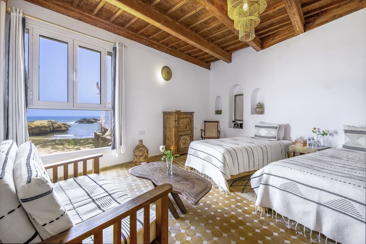Un dormitorio con dos camas, techo de madera, vista al mar y una mesa con un florero.