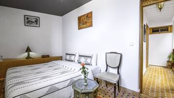 A bedroom with a large bed, a chair, a small table with a vase, and a painting on the wall.