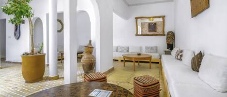A spacious room with a white sofa, a round table, and a potted plant.