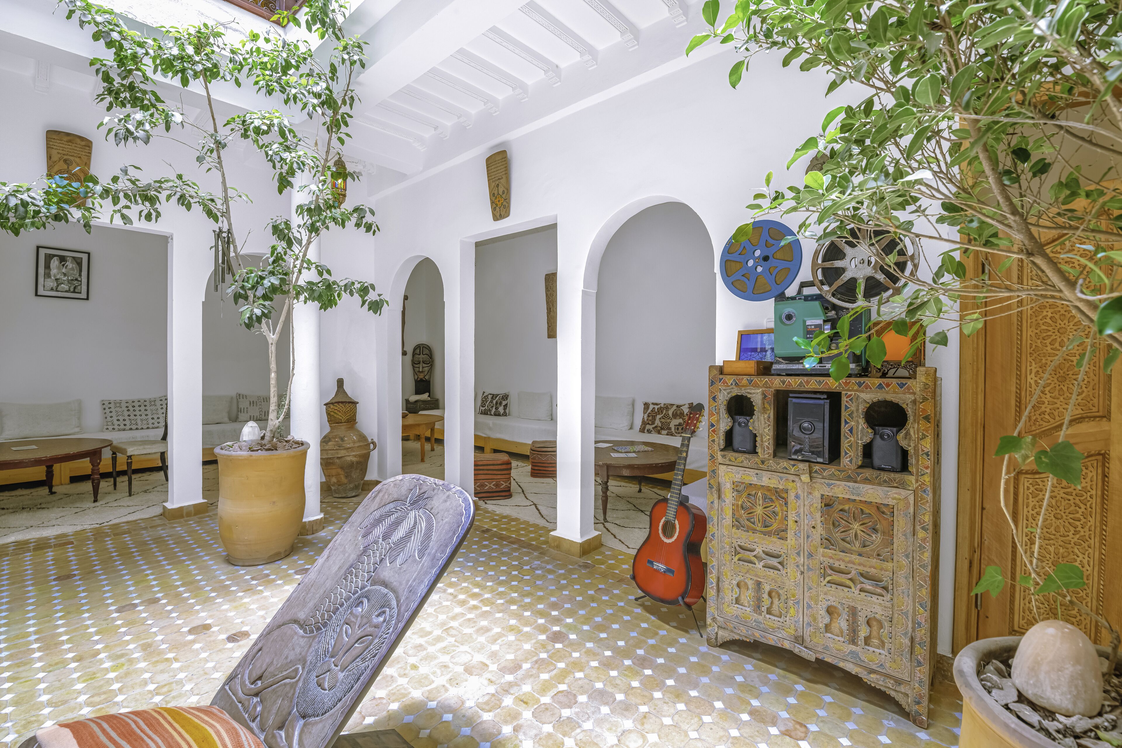 A spacious living area with a patterned floor, a sofa, a guitar, and a decorative cabinet.