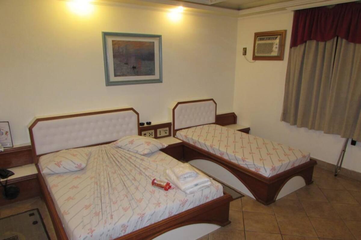 A hotel room with two single beds, a painting on the wall, and a window with curtains.