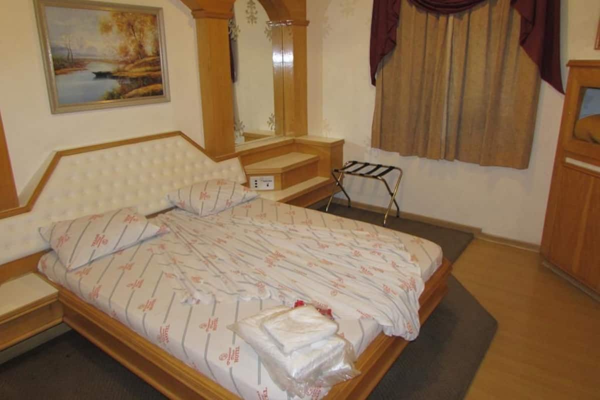 A bedroom with a bed, a mirror, a painting, and a window with curtains.