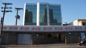 Un hotel moderno con fachada de vidrio reflectante, techo plano y un toldo decorativo con remolinos rojos.
