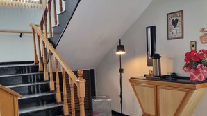 Un vestíbulo de hotel con una escalera, un mostrador de recepción, una decoración de pared con temática de café y un felpudo rojo.