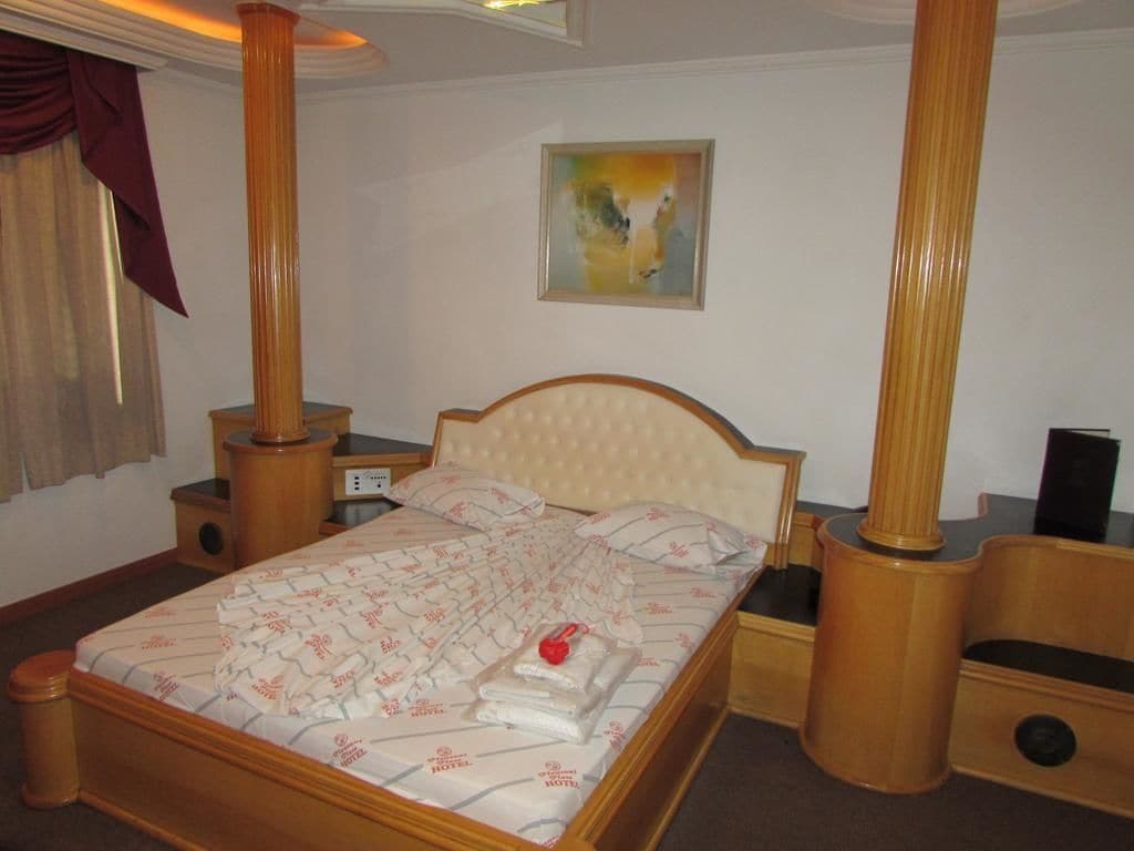 A neatly made bed with a patterned bedspread, wooden nightstands, and a single artwork on the wall.
