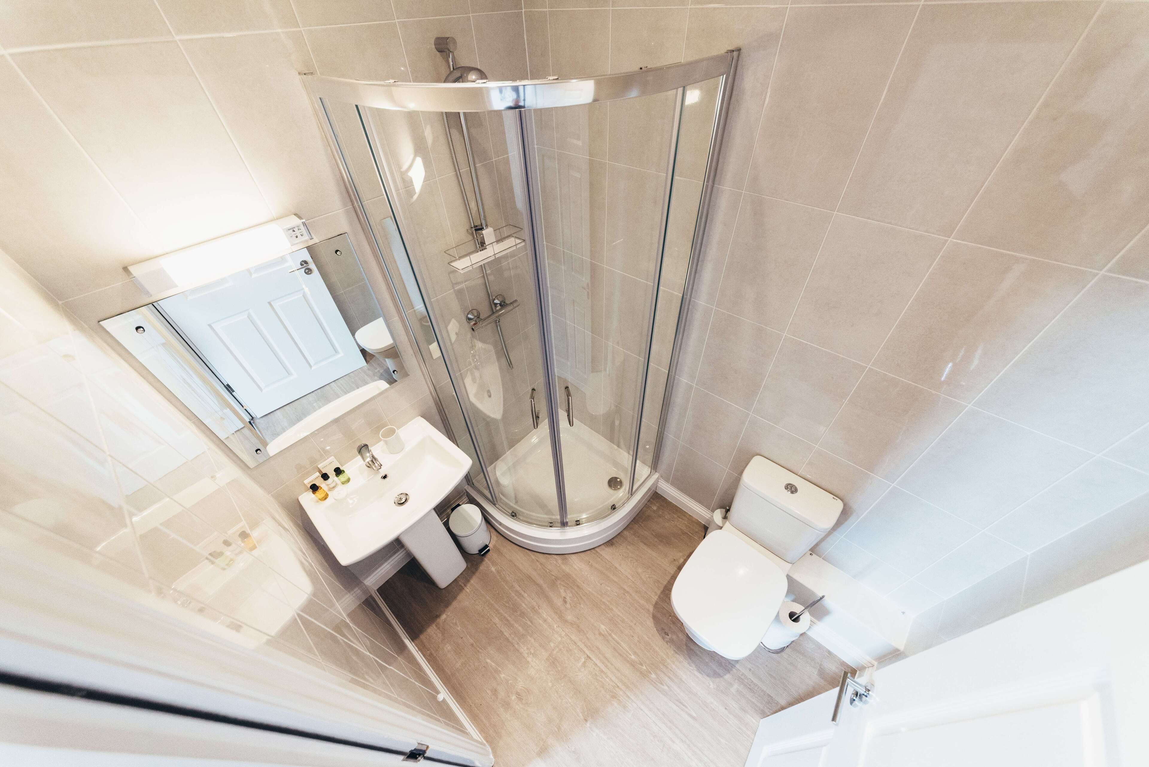 Un baño moderno con ducha de vidrio, lavamanos con espejo e inodoro.