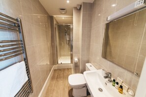 A modern bathroom with a glass-enclosed shower, a white toilet, a sink with toiletries, and a large mirror. - The Stay Company Friar Gate (Derby)