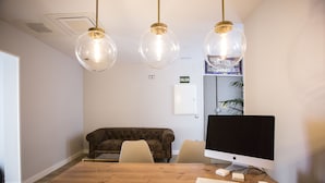 A conference room with a wooden table, two chairs, a brown sofa, and a large Apple monitor. - Hola Rooms (Madrid)