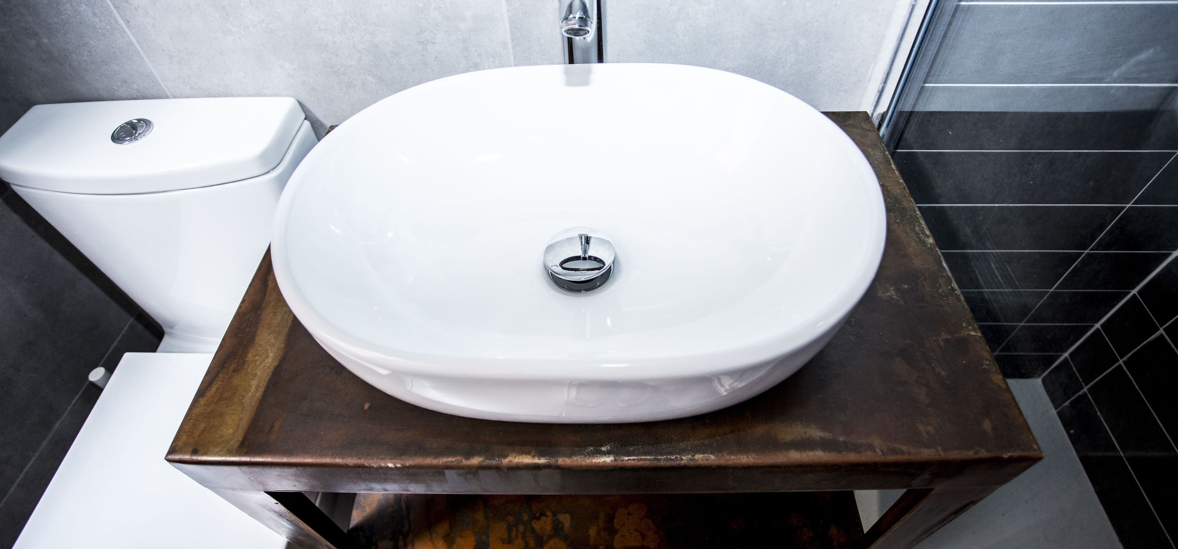 Een badkamer met een wit wastafelmeubel, een toilet en zwart betegelde muren.