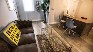 A modern living room with a sofa, a coffee table, a rug, and a desk with chairs. - Hola Rooms (Madrid)
