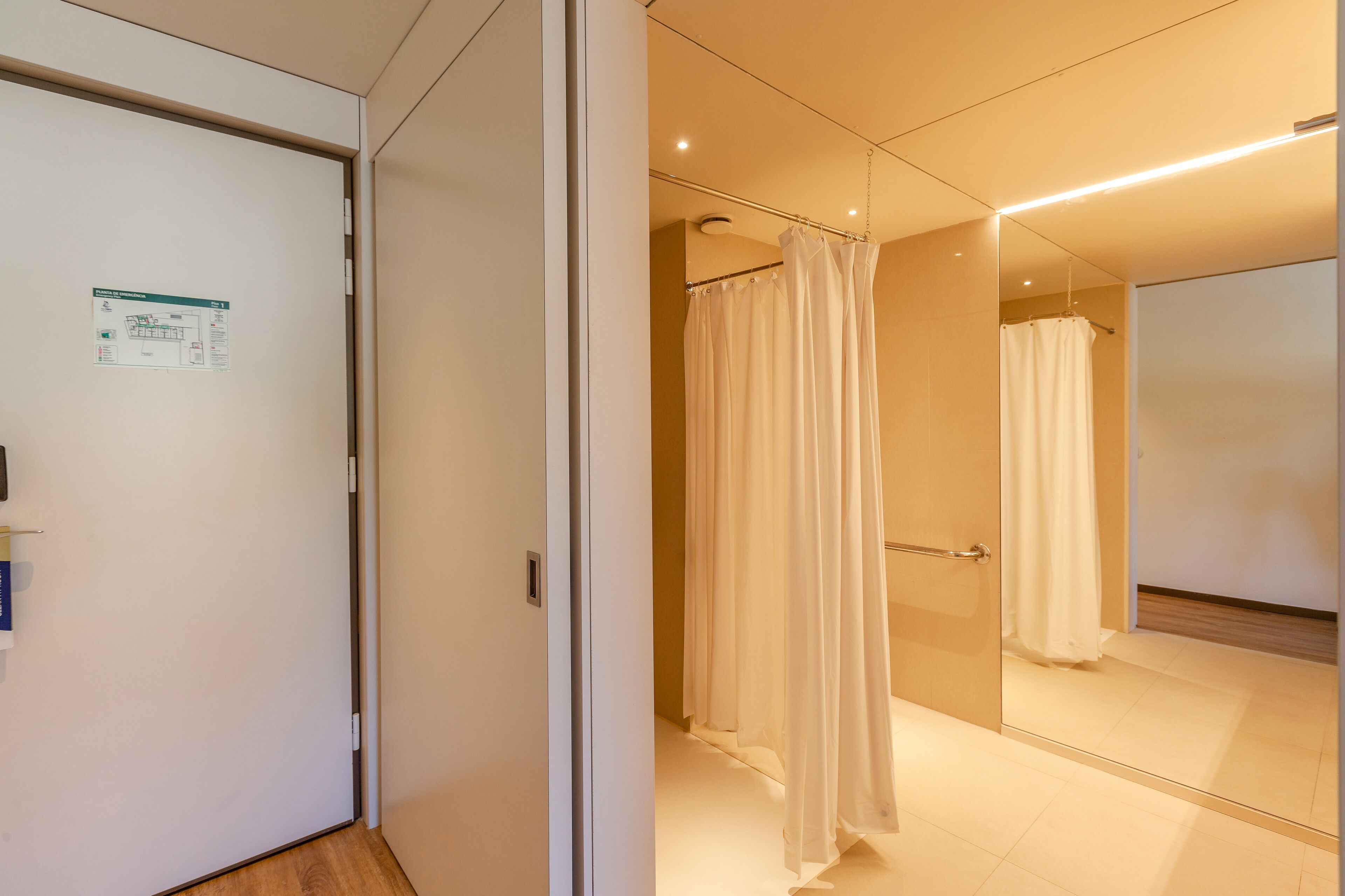 Une chambre d’hôtel moderne avec un grand miroir, un rideau de douche et une porte avec une pancarte.