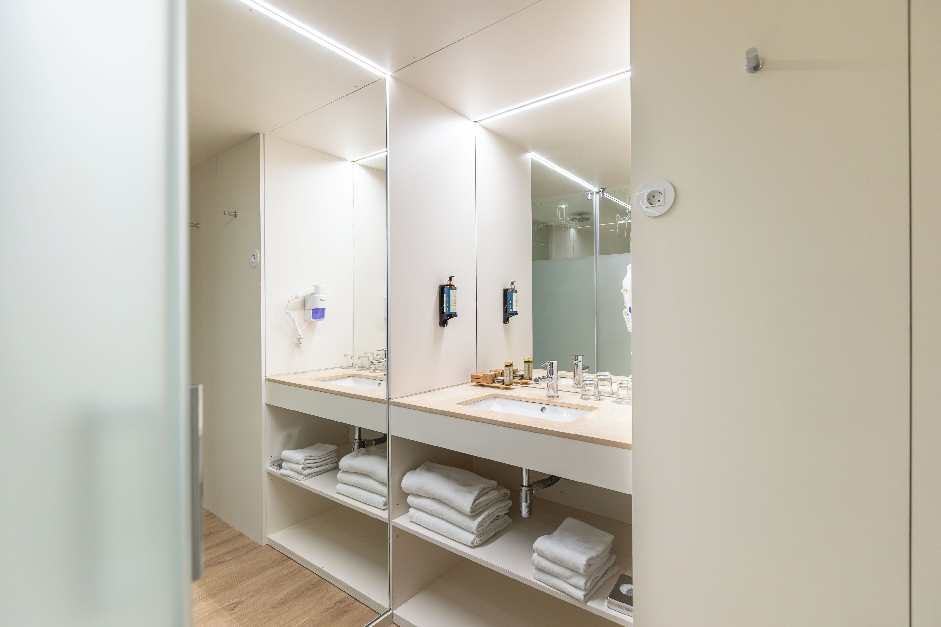 Un baño moderno con un espejo grande, dos lavamanos y una zona de ducha.