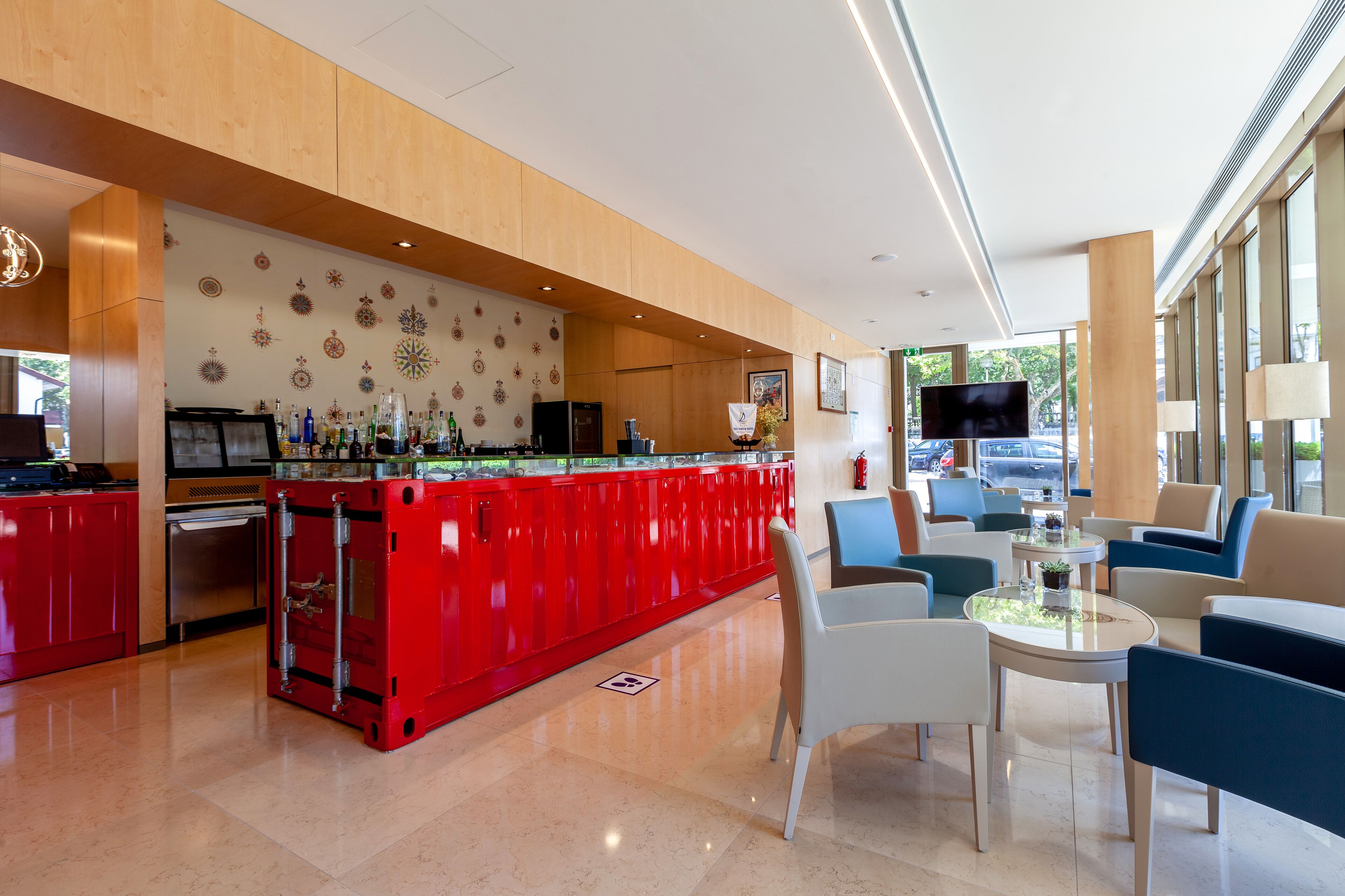 A modern hotel lobby with a red bar area, seating, and a large TV screen.
