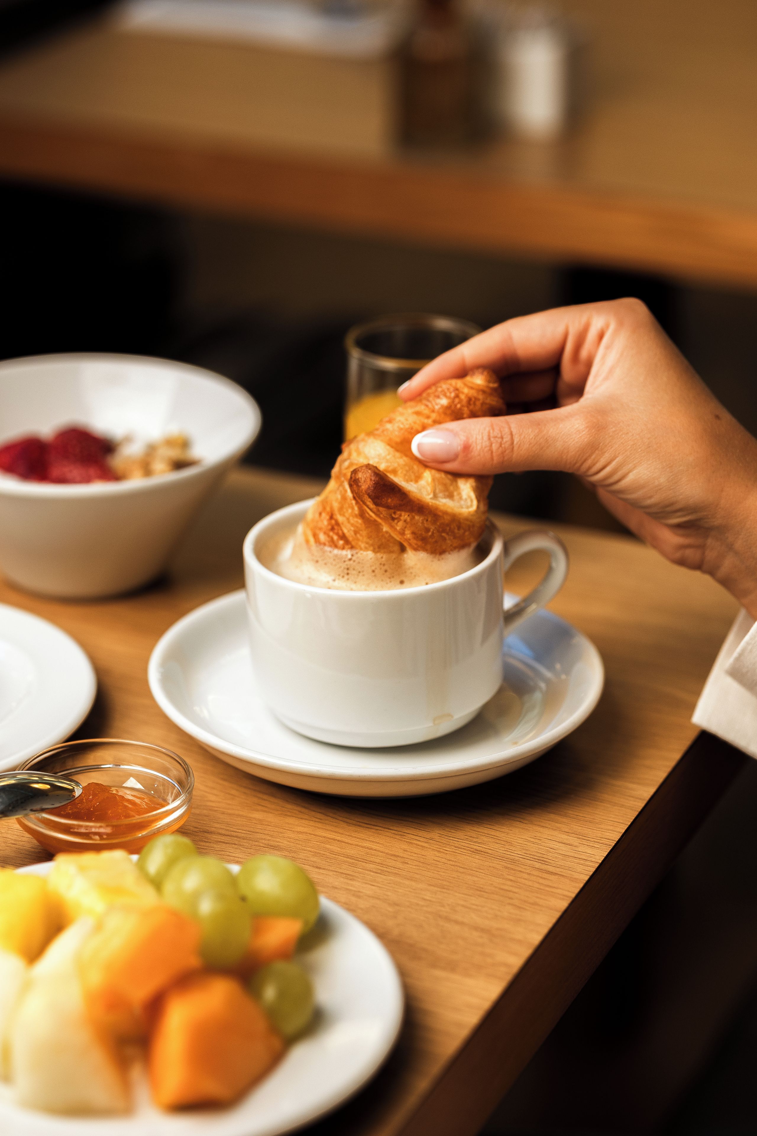 Un desayuno con una taza de café, un croissant y una bandeja de fruta.