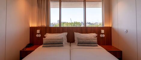 A double bed with patterned pillows, a bedside phone, and a window with a view of buildings and trees.