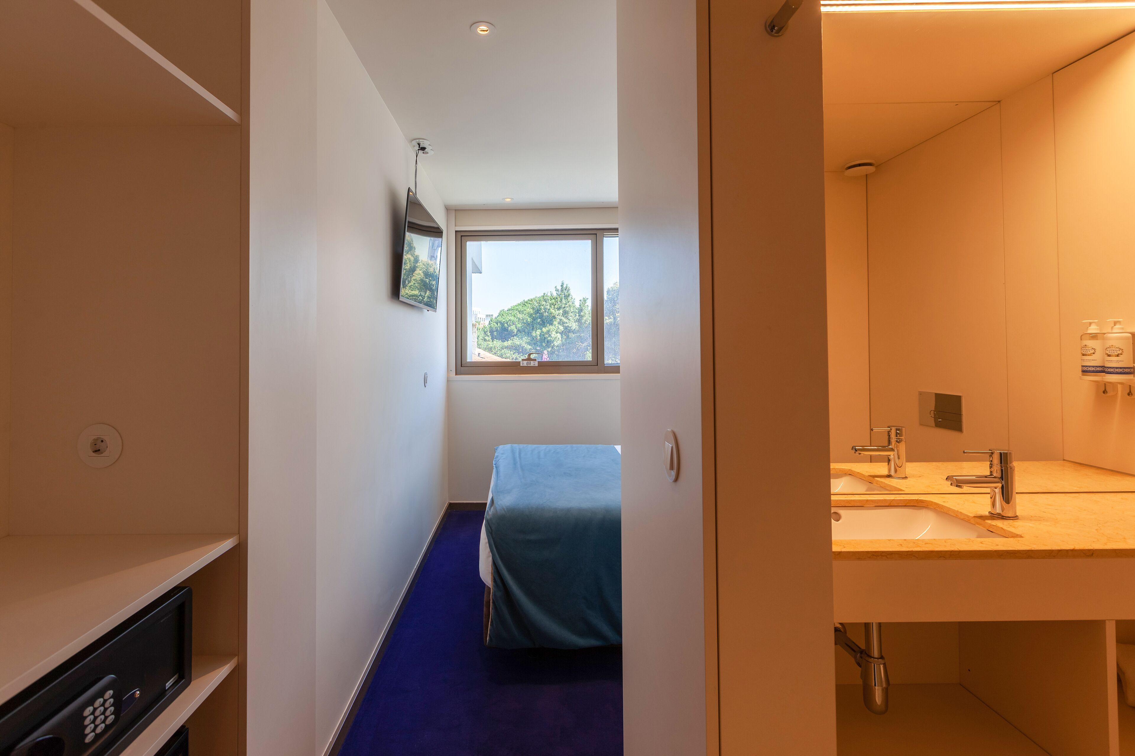 A modern hotel room with a bed, a large window, a sink, and a television.