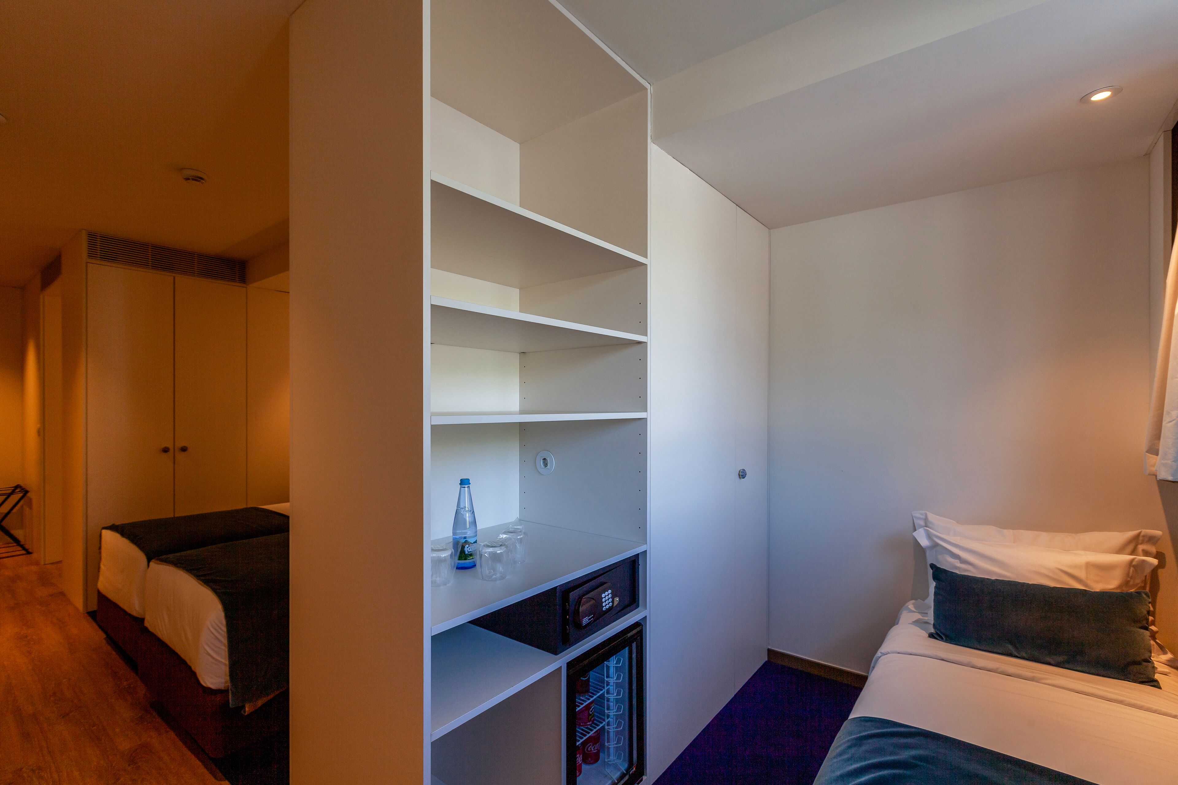 Une chambre d’hôtel de taille réduite, dotée d’un lit simple, d’une armoire intégrée et d’un mini-bar.