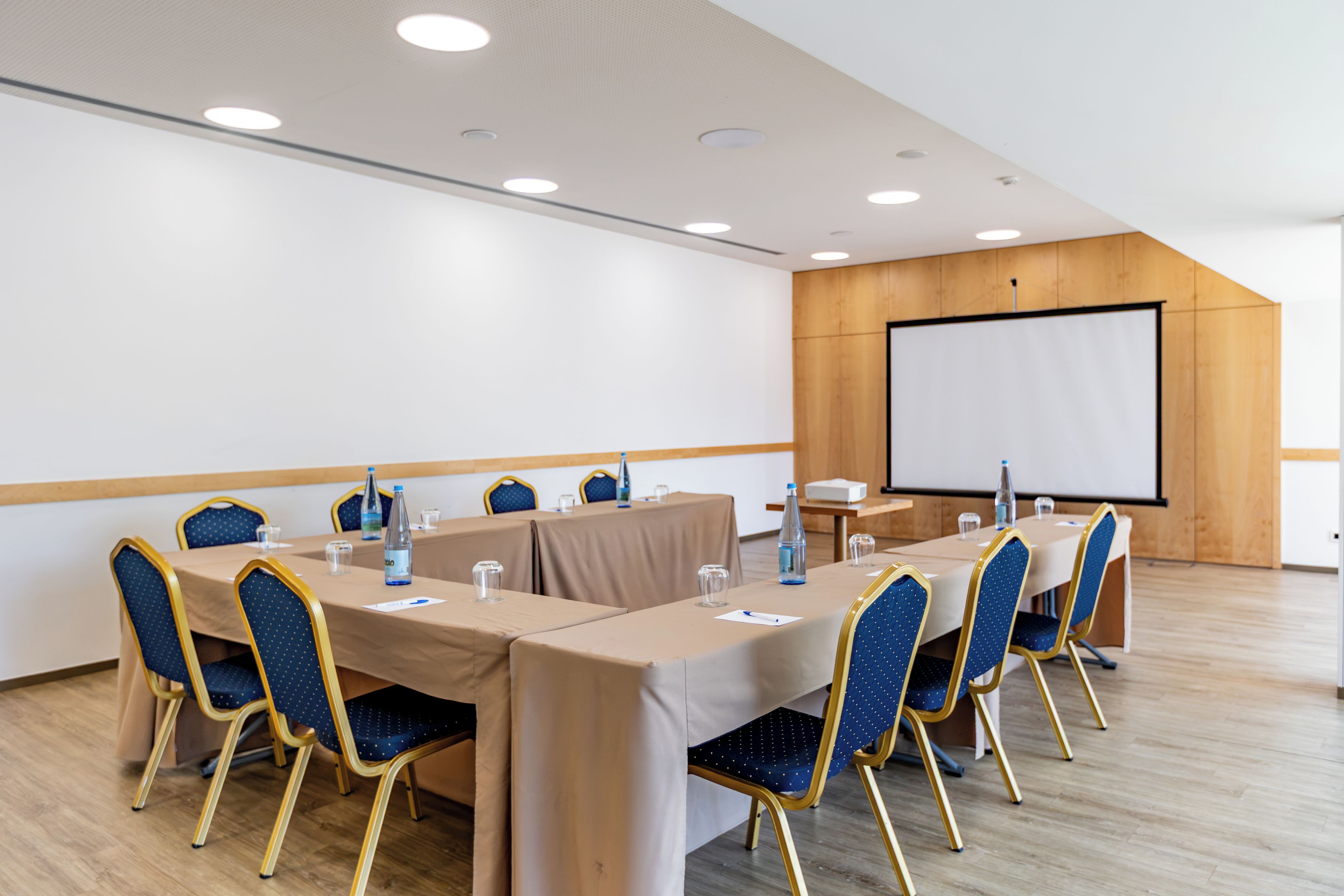 A conference room with a long table, chairs, a projector screen, and a whiteboard.