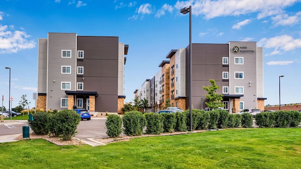 Un immeuble résidentiel moderne à plusieurs étages, doté d’un toit plat, d’un espace de stationnement et d’une pelouse bien entretenue.