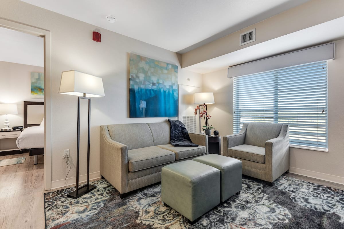 A modern living room with a sofa, ottoman, floor lamp, and a painting on the wall.