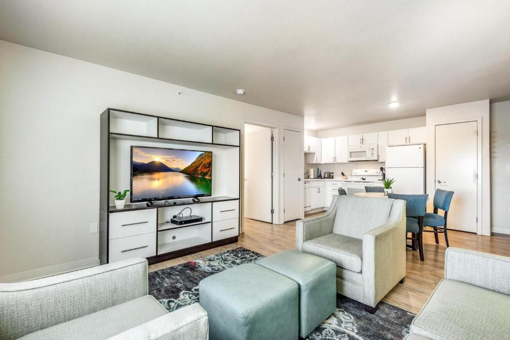A modern living room with a flat-screen TV, a sofa, a coffee table, and a dining area with chairs.