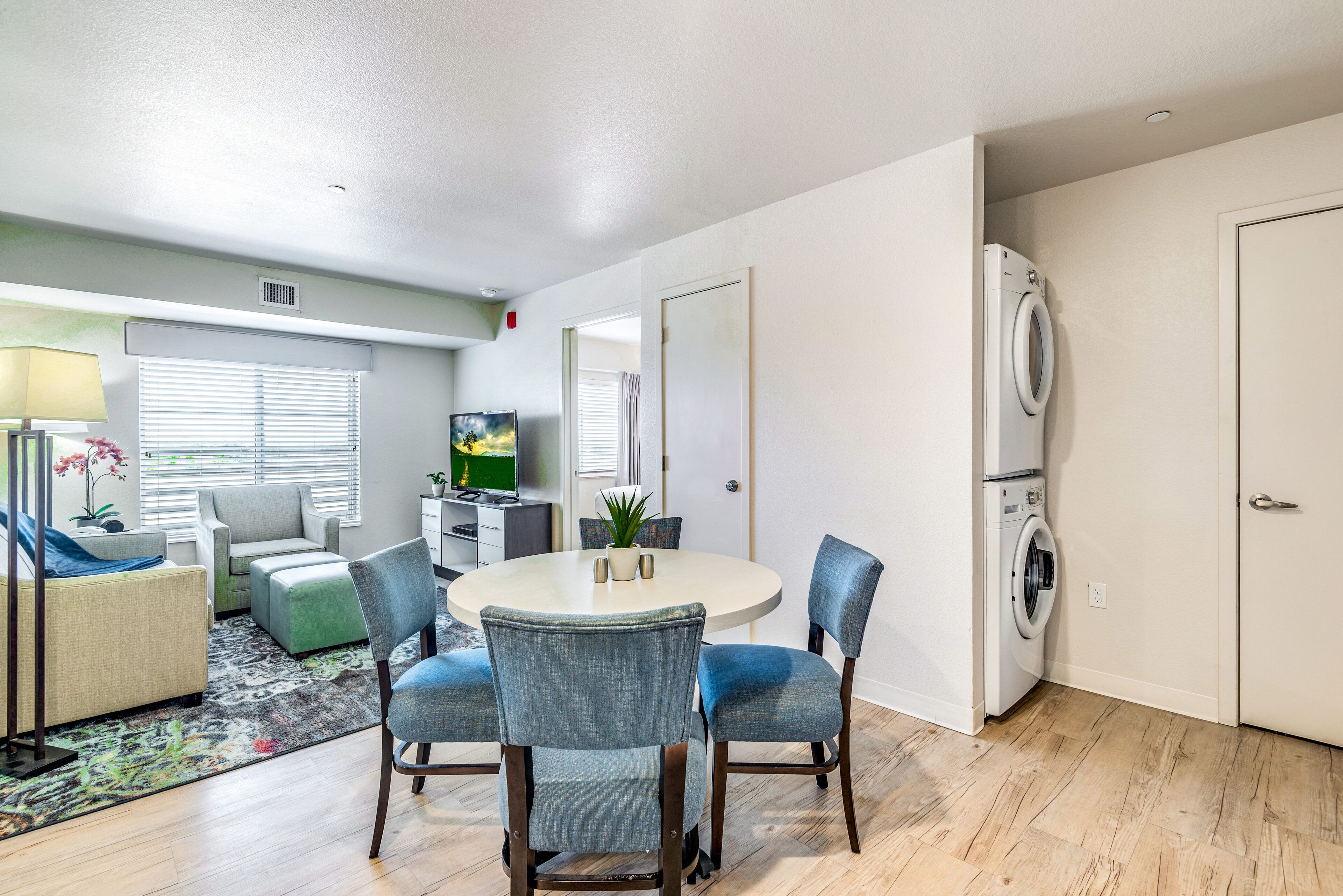 A modern living room with a round dining table, blue chairs, a sofa, a TV, and a washing machine.