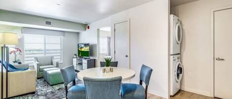 A modern living room with a round dining table, blue chairs, a sofa, a TV, and a washing machine.