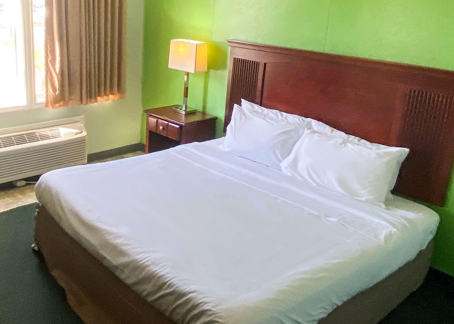 Una cama bien hecha con ropa blanca en una habitación con paredes verdes y cabecera de madera.