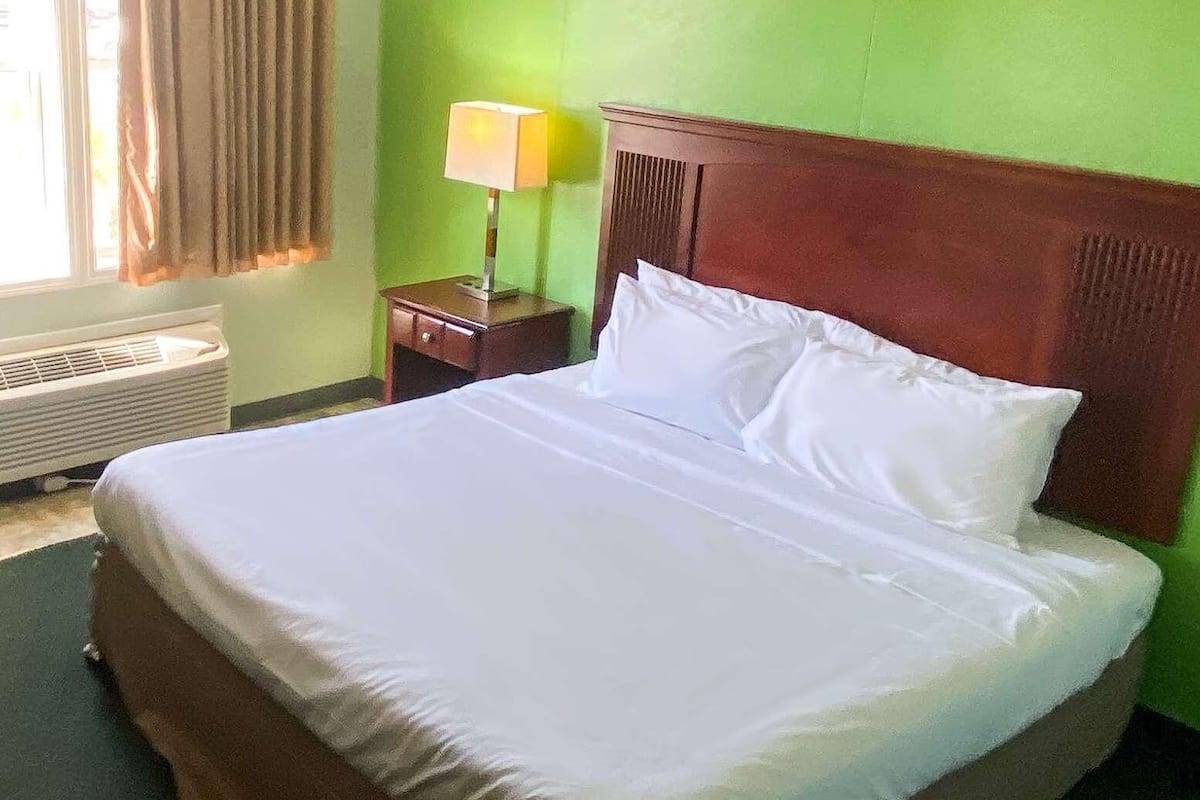 Una cama bien hecha con ropa blanca en una habitación con paredes verdes y cabecera de madera.