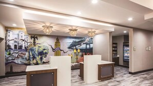 A hotel lobby with a mural, reception desks, and a vending machine. - La Quinta Inn & Suites by Wyndham Baton Rouge - Port Allen (Port Allen)