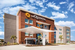 Un hotel La Quinta con un diseño moderno, que presenta un llamativo logo de sol, múltiples ventanas y una entrada cubierta.
