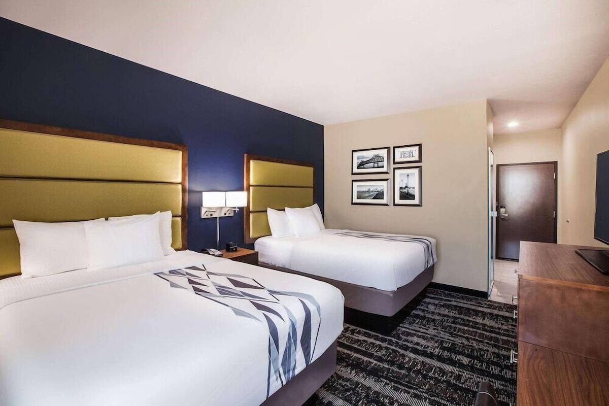 Une chambre d’hôtel avec deux lits, un bureau, une chaise, une télévision et des tableaux encadrés au mur.