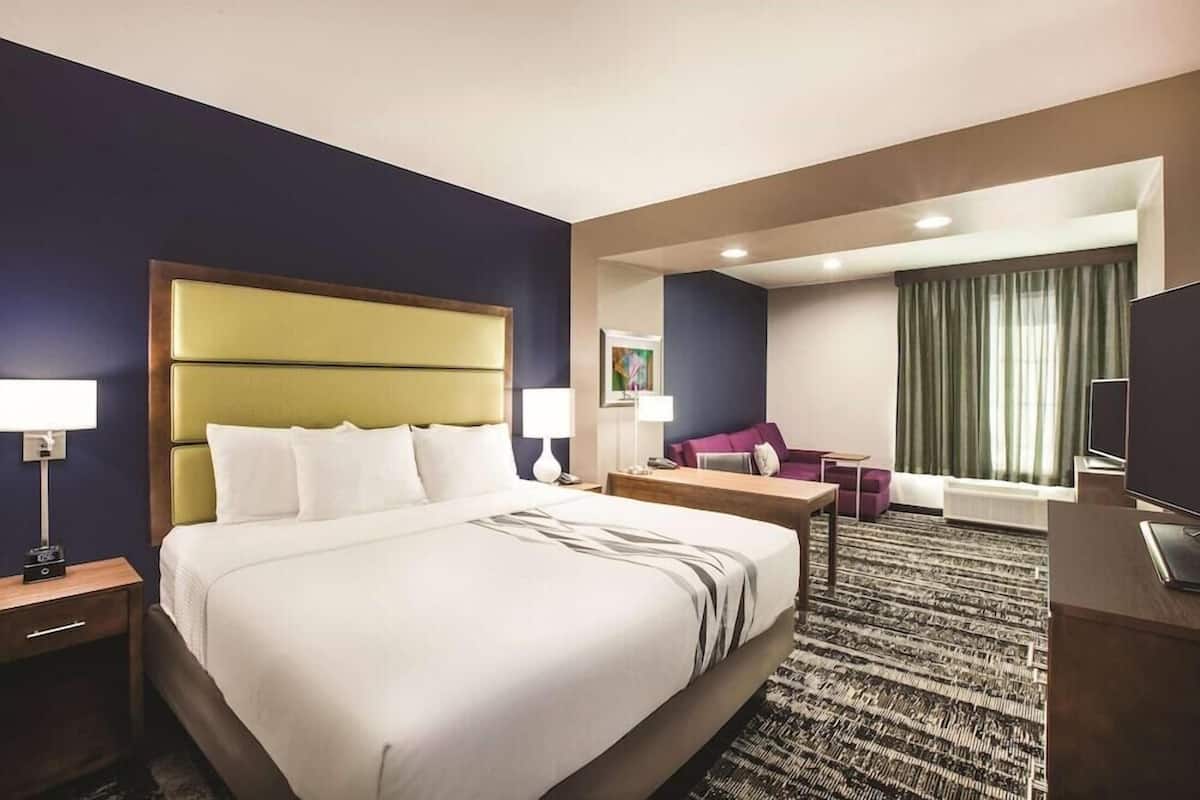 Une chambre d’hôtel avec un grand lit, un bureau, une chaise, une télévision et une fenêtre avec des rideaux.