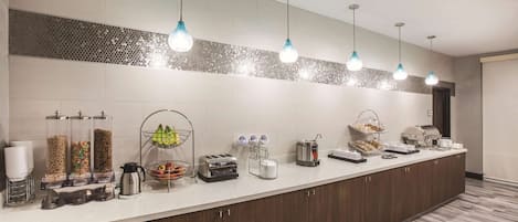 A hotel kitchen with a long counter, various food items, and kitchen appliances.