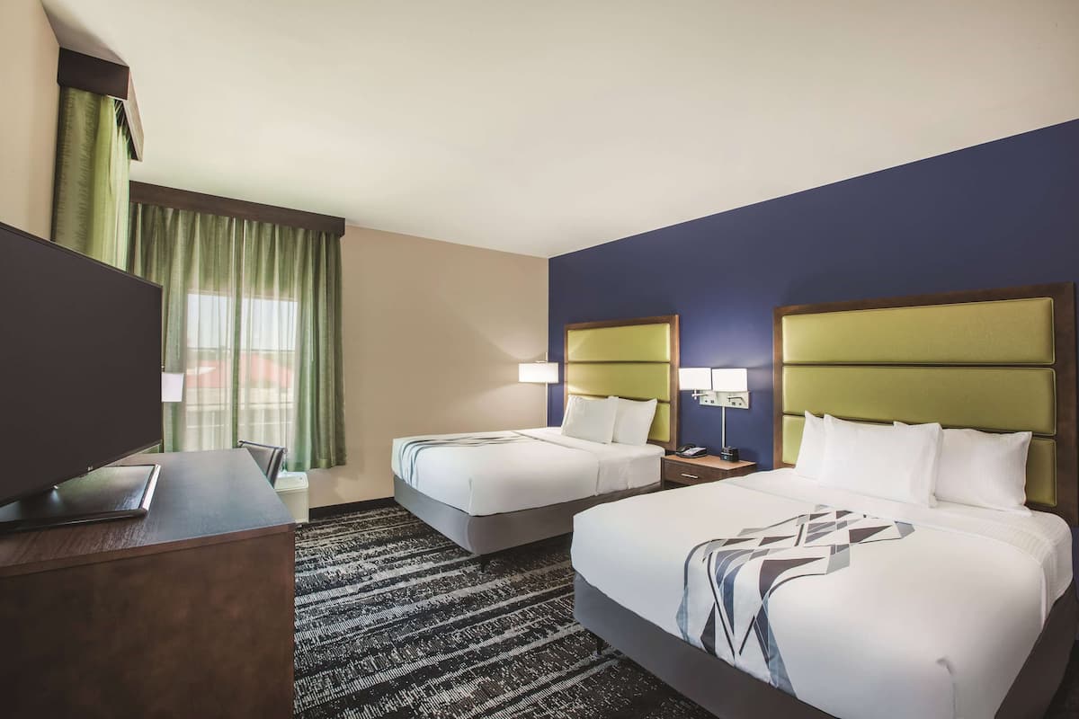 Une chambre d’hôtel avec deux lits, un bureau, une télévision et une fenêtre avec des rideaux.